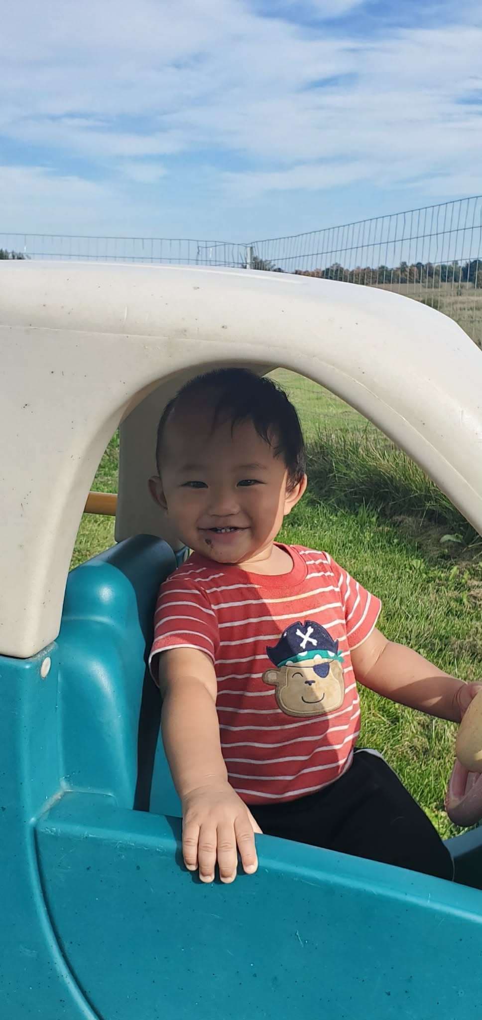 Portrait of a smiling child sitting in a small toy car outdoors.