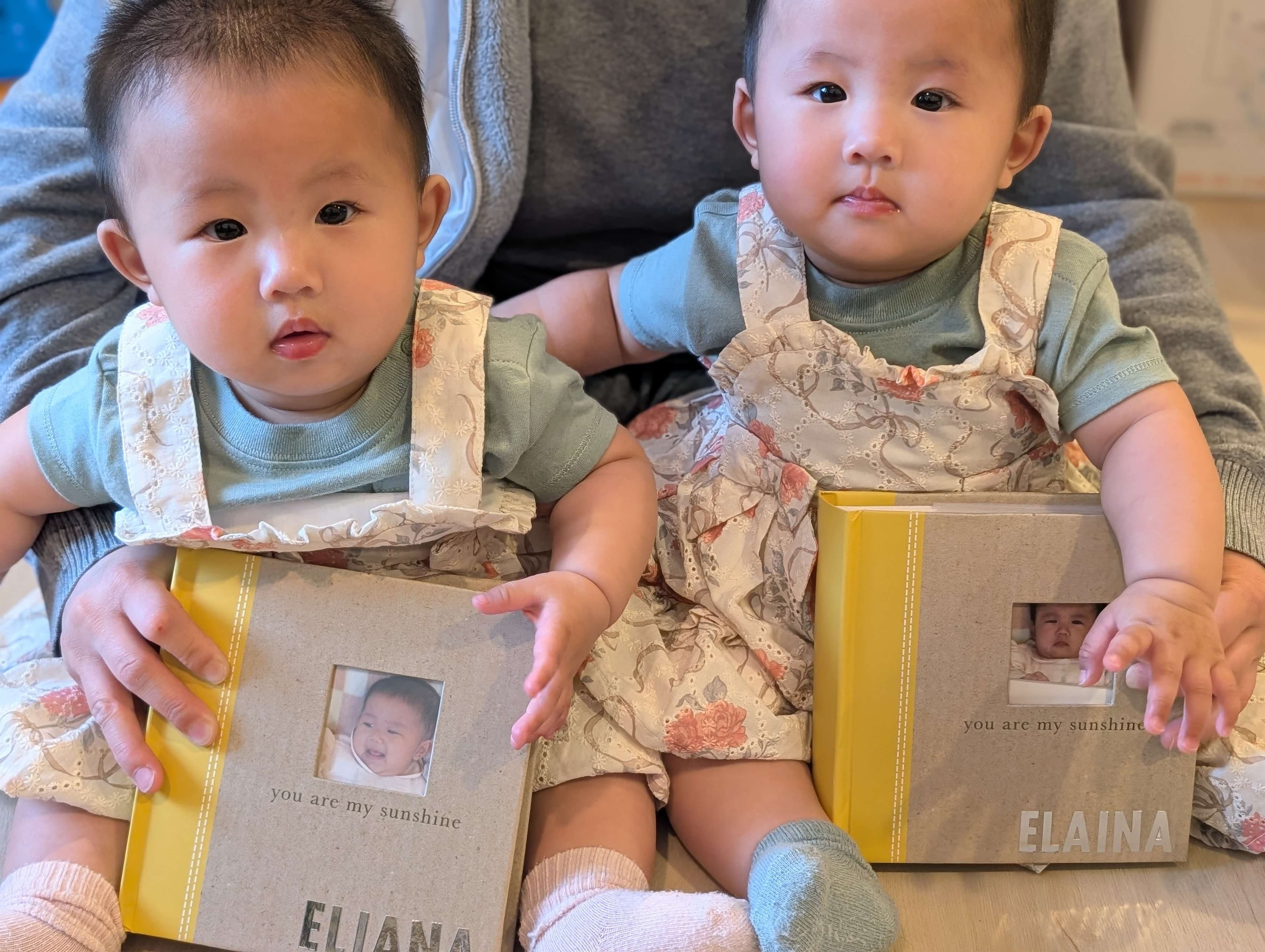 Portrait of twin children sitting together and holding photo books indoors.