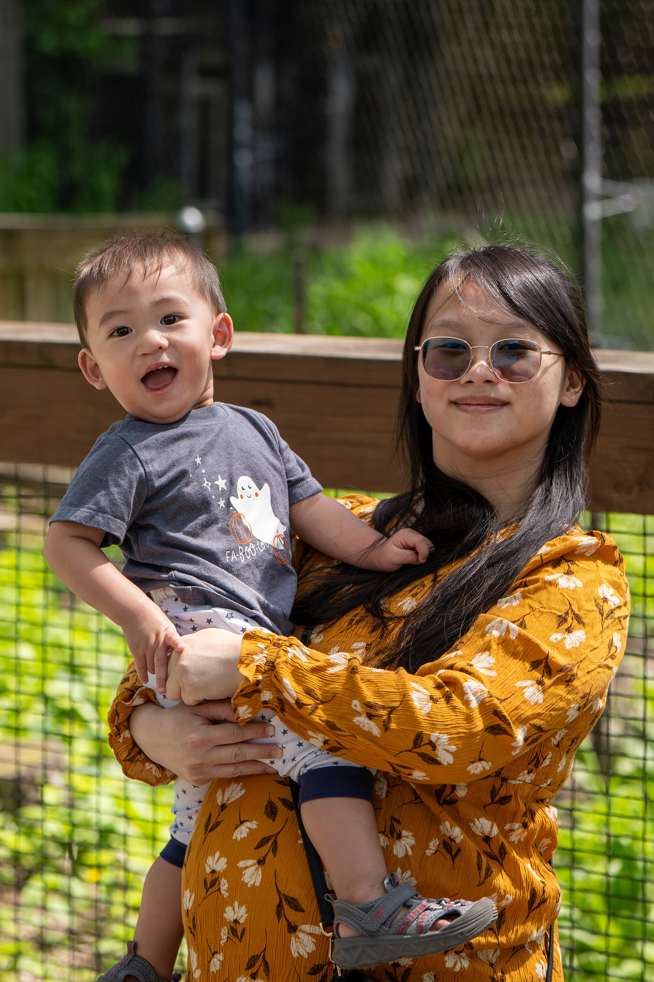 Portrait of a woman holding a smiling child outdoors in bright daylight.