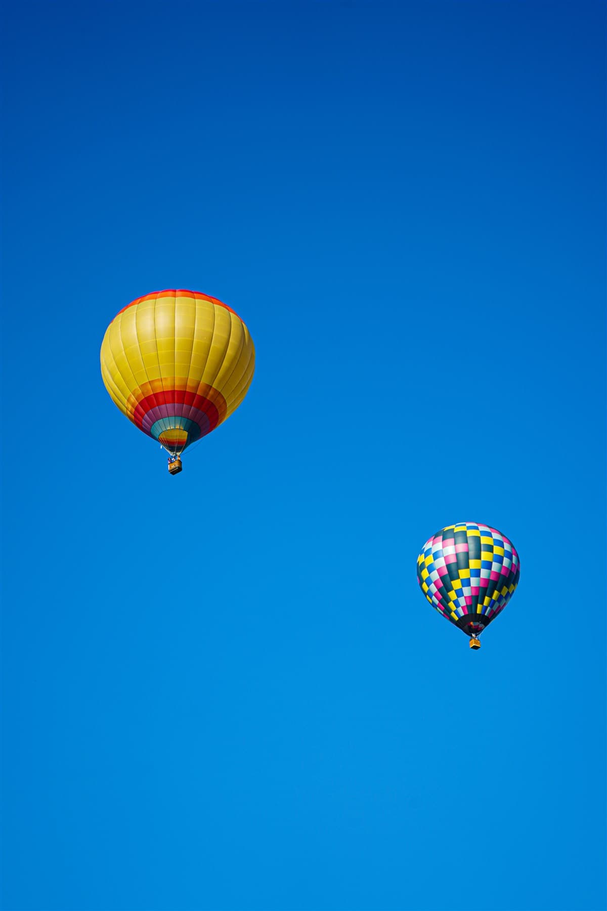 Two hot air balloons floating in wide blue sky.