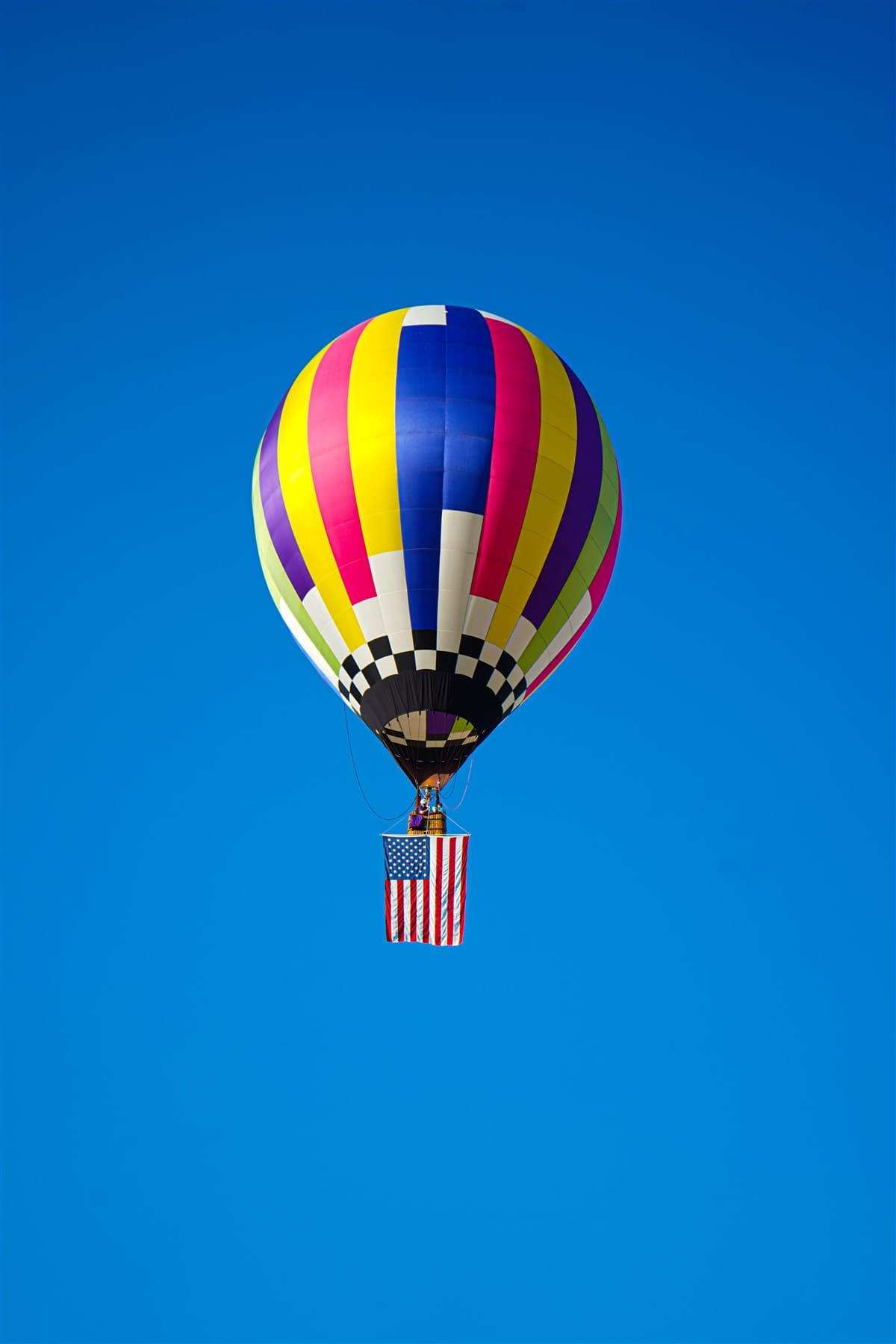 Single rainbow hot air balloon against a clear blue sky