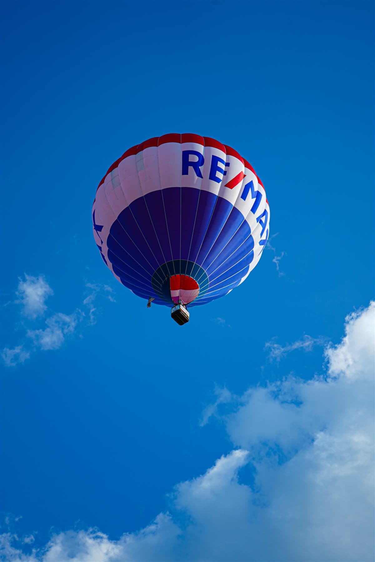 Single red hot air balloon against bright blue sky and white cloud.