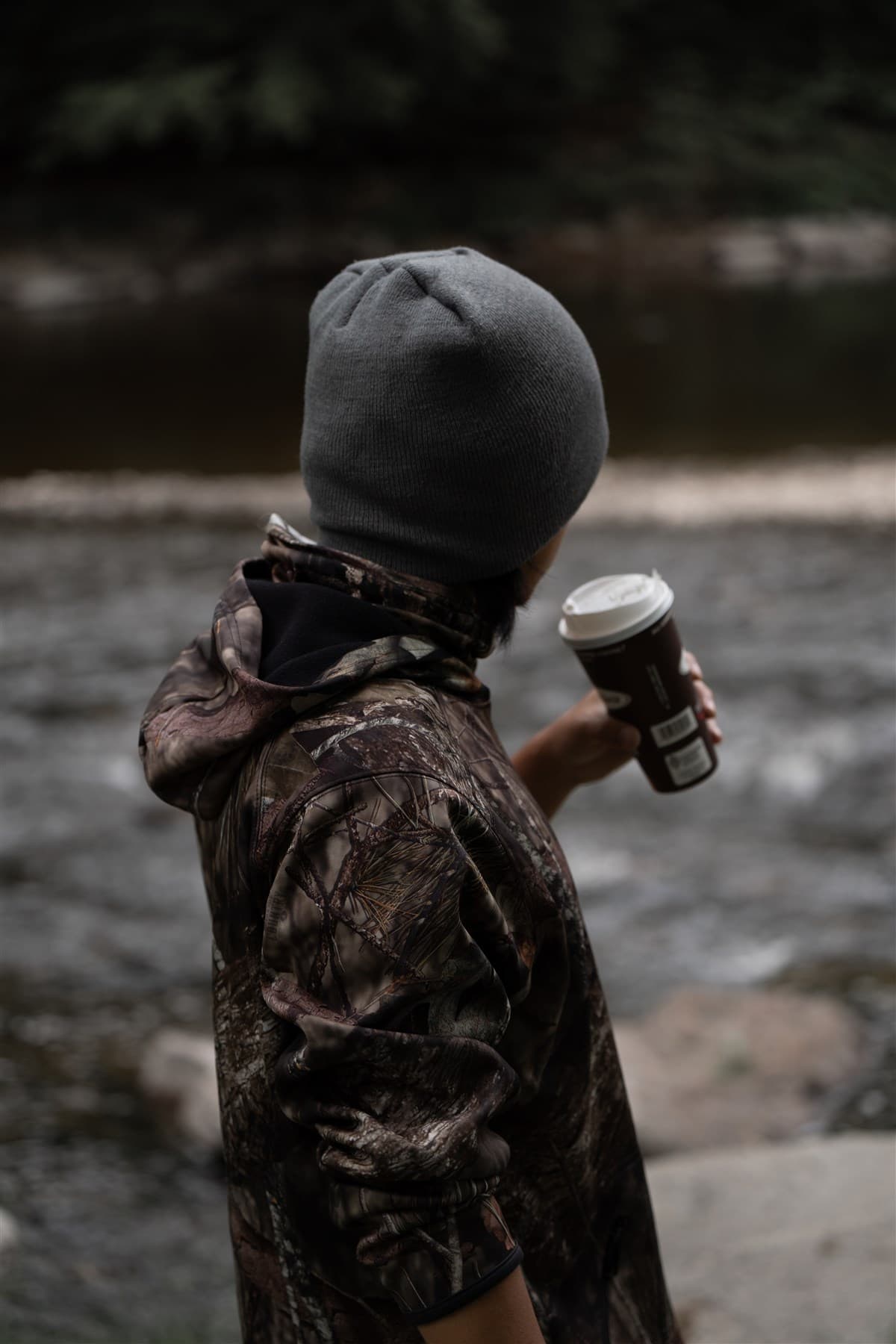 Figure standing near the water in an outdoor setting.