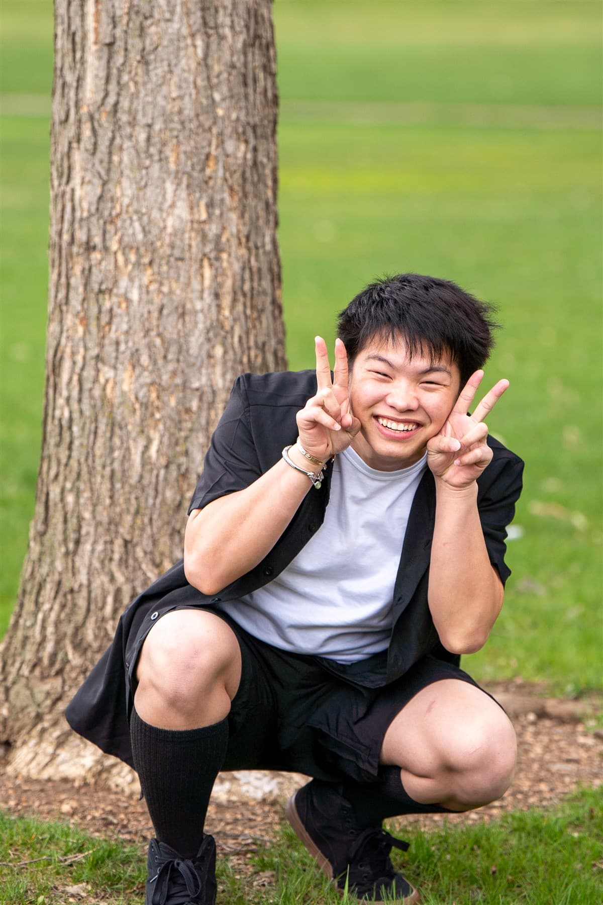 Playful portrait crouching beside a tree in a park.