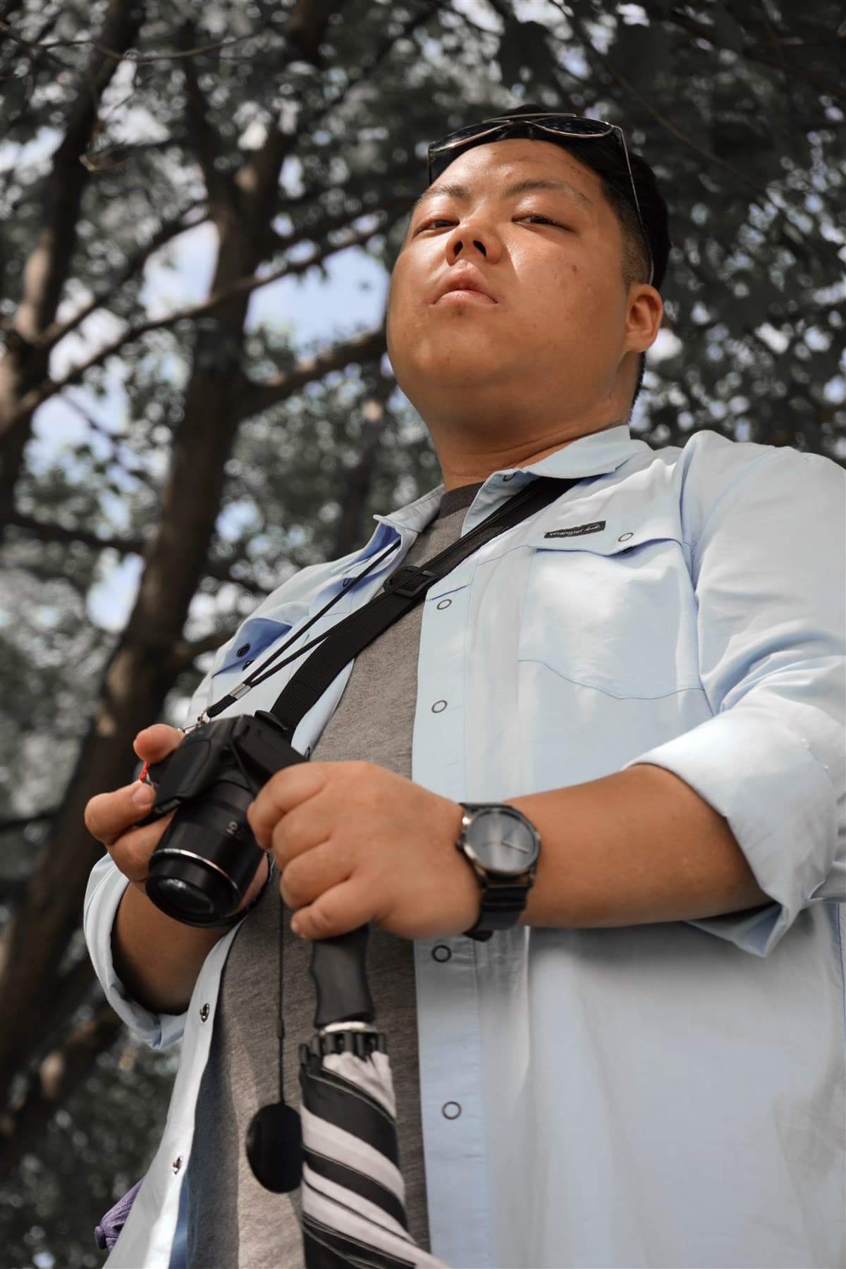 Low-angle portrait holding a camera under tall trees.