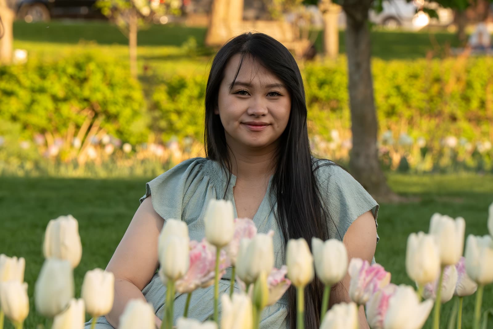 Portrait seated behind tulips in a garden at golden hour.