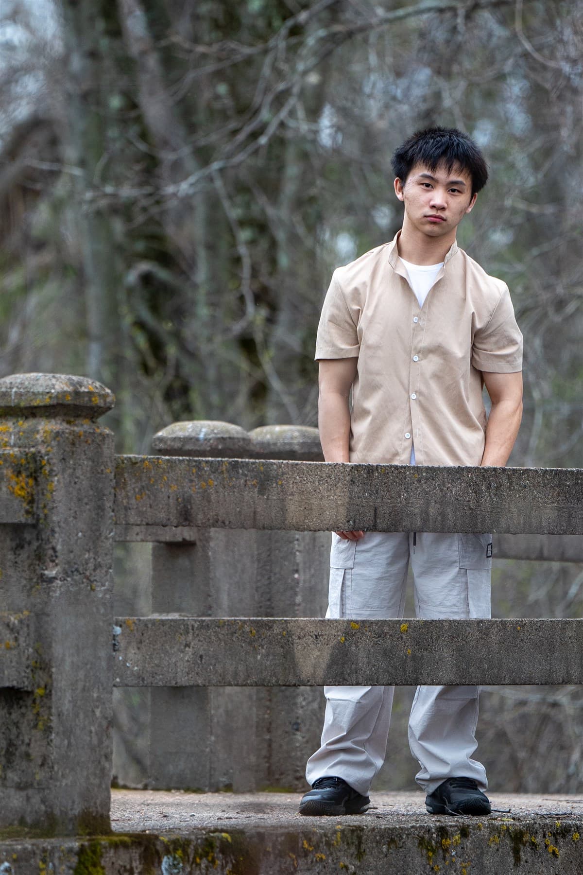 Portrait beside a weathered bridge in a wooded setting.